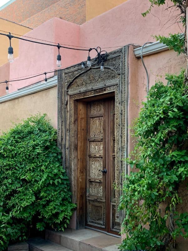 Beautiful Rustic Door With Lights On Top And Green Bushes On The Sides